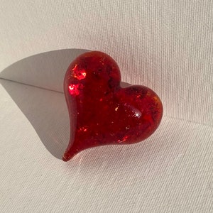 May include: A red glass heart with a sparkly finish. The heart is slightly misshapen and has a pointed bottom.