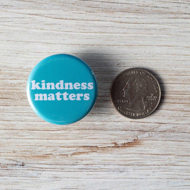 Pu&ograve; includere: Un bottone blu con il testo "kindness matters" in lettere bianche. Il bottone &egrave; accanto a una moneta da 25 centesimi di dollaro americano per riferimento alle dimensioni.