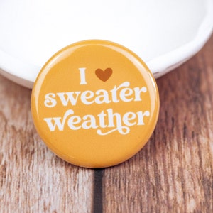 May include: A yellow button with the text "I ♥ sweater weather" in white.