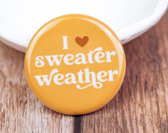 May include: A yellow button with the text "I ♥ sweater weather" in white.
