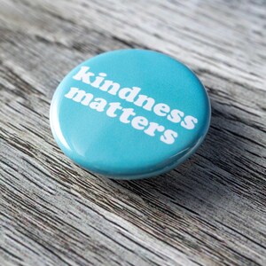 Pu&ograve; includere: Un bottone blu con il testo "kindness matters" in lettere bianche.