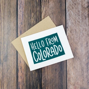 May include: A white card with a green rectangle that says "Hello from Colorado" in white text. The card is on top of a brown envelope.