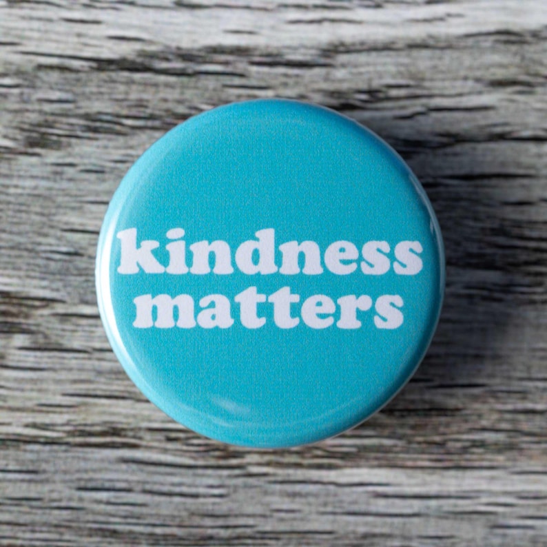 Pu&ograve; includere: Un bottone blu con il testo "kindness matters" in bianco.