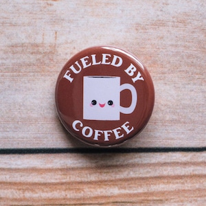 May include: A brown button with white text that reads "Fueled by Coffee" and a white cartoon coffee mug with a smiling face.