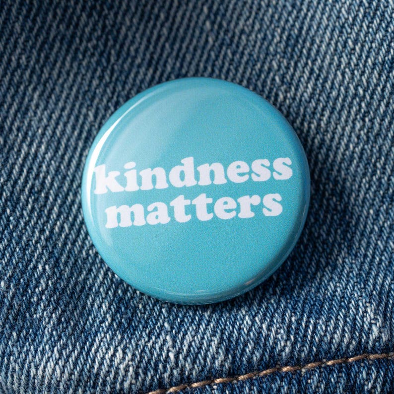 Pu&ograve; includere: Un bottone blu con il testo "kindness matters" in lettere bianche.