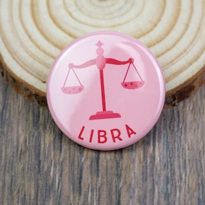 May include: Pink round button with a pink Libra zodiac symbol and the word "LIBRA" in red letters.