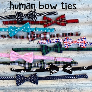 Peut inclure: Une collection de 10 nœuds papillon colorés avec différents motifs, y compris des étoiles, du tartan et des crânes. Les nœuds papillon sont disposés en rangée sur une surface texturée. Le texte "human bow ties" est écrit au-dessus des nœuds papillon.