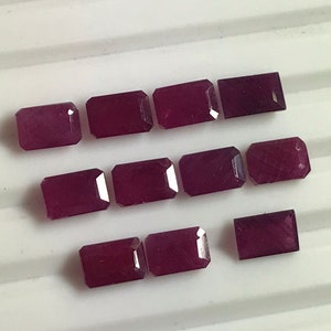 Può includere: Una collezione di dodici pietre preziose rettangolari sfaccettate. Le pietre preziose sono di un colore viola profondo e ricco.