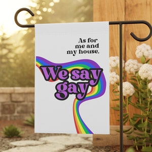 May include: A white garden flag with a rainbow and the text "As for me and my house, We say gay".