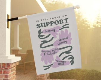 May include: A white house flag with the words "in this house we SUPPORT" in black text. Below, in a floral design, are the words "decency", "factual history", "diversity, equity, & inclusion", and "common sense" in a purple font.