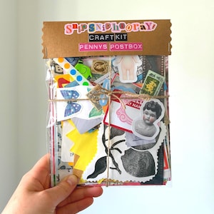 Puede incluir: Un kit de manualidades envuelto en celofán transparente, con una cabecera de cartón marrón que dice "SHIPS NIPHOORAY CRAFT KIT PENNYS POSTBOX". El kit contiene varias pegatinas y efímeras coloridas, atadas con hilo.