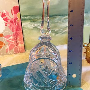 Puede incluir: Una campana de cristal transparente con un mango largo y facetado. La campana tiene un diseño grabado detallado de un pájaro y follaje. La campana mide aproximadamente 13 cm de altura.
