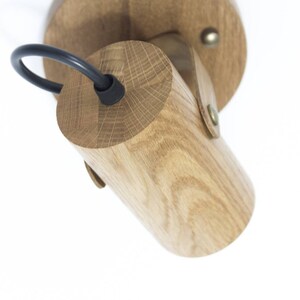 May include: A wooden wall sconce with a black cord and a round wooden base. The sconce is made of natural wood and has a rustic look.