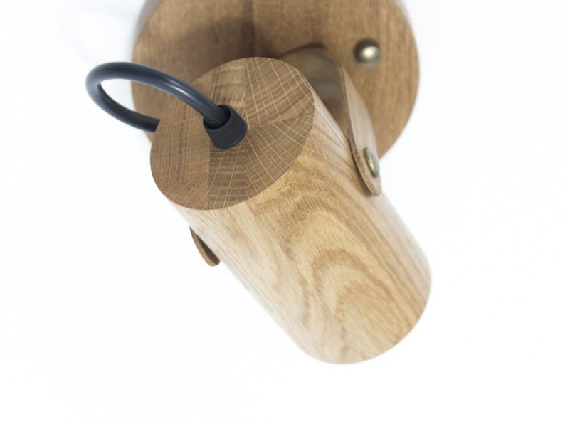 May include: A wooden wall sconce with a black cord and a round wooden base. The sconce is made of natural wood and has a rustic look.