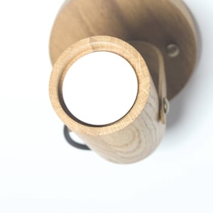 May include: A wooden wall sconce with a round light fixture. The sconce is made of natural wood and has a simple, modern design.