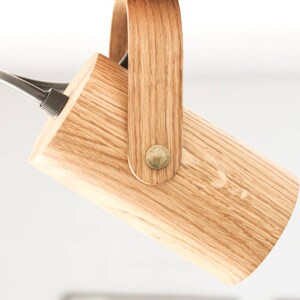 May include: A wooden pendant light fixture with a cylindrical shade and a wooden handle. The fixture is suspended from the ceiling by a black cord.