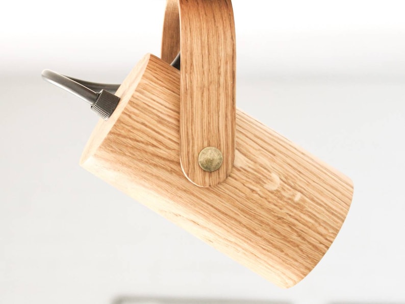 May include: A wooden pendant light fixture with a cylindrical shade and a wooden handle. The fixture is suspended from the ceiling by a black cord.