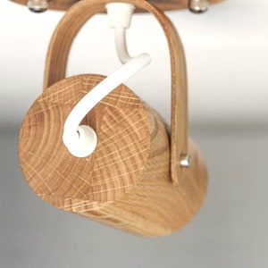 May include: A wooden ceiling light fixture with a natural wood finish and a white cord. The light fixture has a simple design and is made of a single piece of wood.