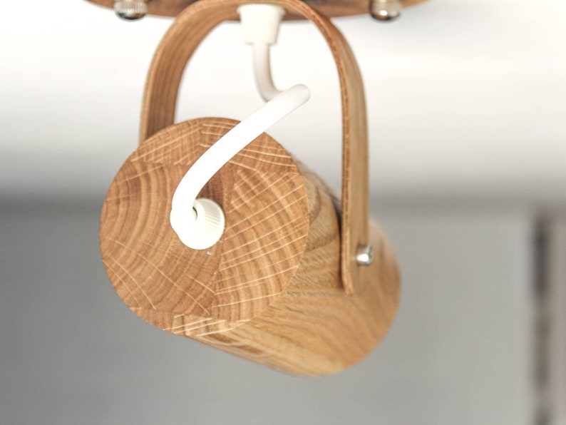 May include: A wooden ceiling light fixture with a natural wood finish and a white cord. The light fixture has a simple design and is made of a single piece of wood.