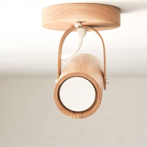May include: A wooden ceiling light fixture with a cylindrical shade and a white diffuser. The light is mounted on a circular wooden base with a leather strap.