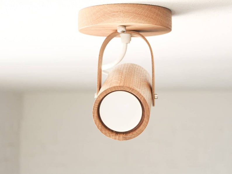 May include: A wooden ceiling light fixture with a cylindrical shade and a white diffuser. The light is mounted on a circular wooden base with a leather strap.