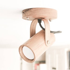May include: A wooden ceiling light fixture with a cylindrical shade and a black cord. The light is mounted to the ceiling with a circular wooden base.