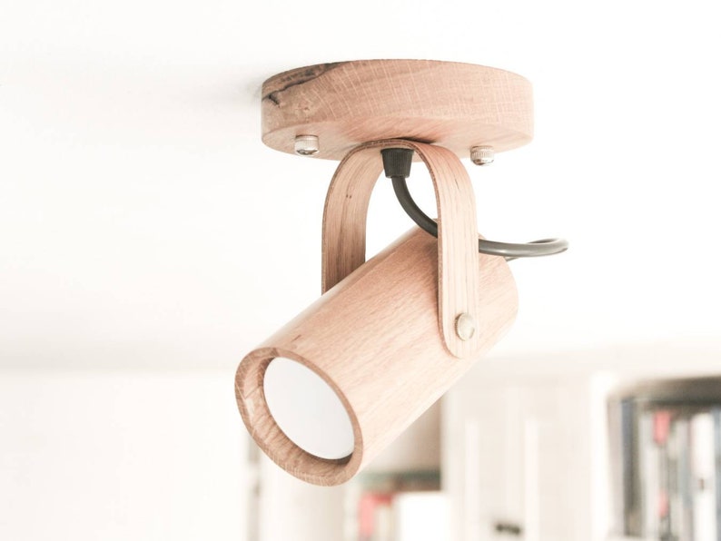May include: A wooden ceiling light fixture with a cylindrical shade and a black cord. The light is mounted to the ceiling with a circular wooden base.