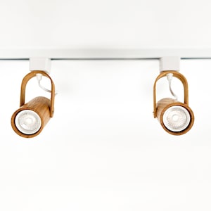 May include: Two wooden track lights with white bulbs, mounted on a white ceiling track.