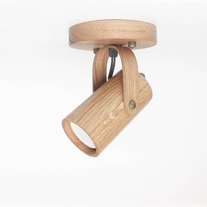 May include: A wooden ceiling light fixture with a cylindrical shade that can be adjusted. The fixture is made of natural wood and has a simple, modern design.
