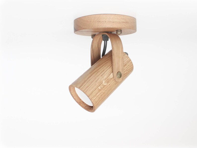 May include: A wooden ceiling light fixture with a cylindrical shade that can be adjusted. The fixture is made of natural wood and has a simple, modern design.