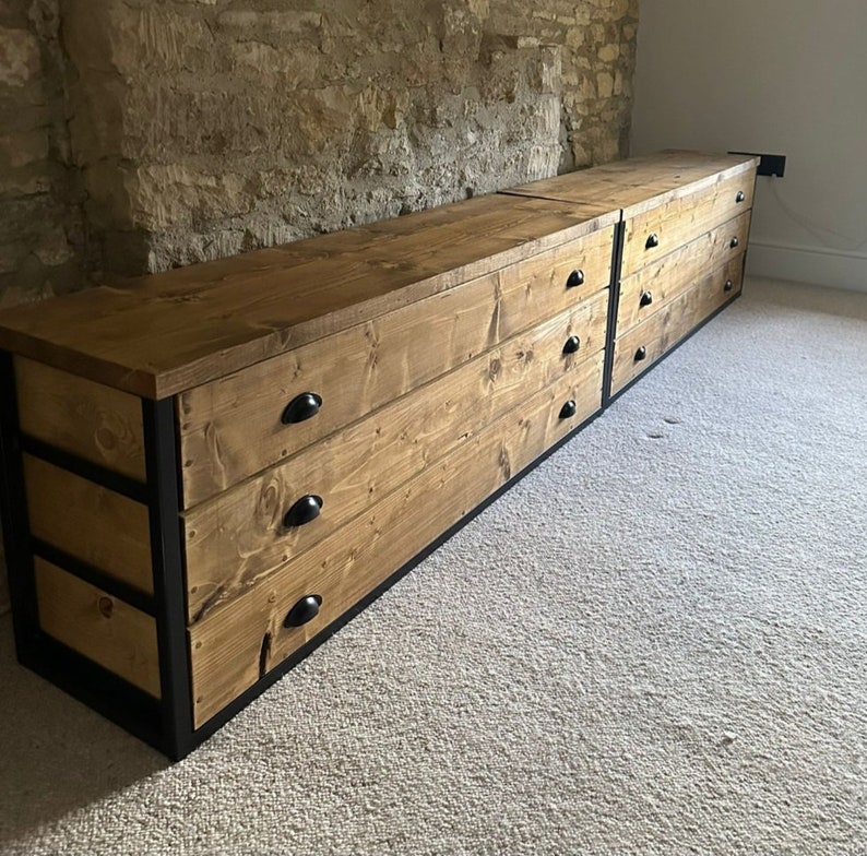 May include: A long wooden dresser with three drawers and black metal accents. The dresser is made of reclaimed wood and has a rustic look.