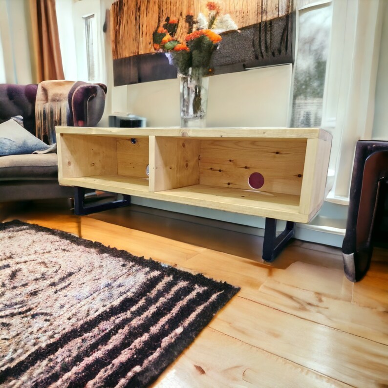 May include: A light wood TV stand with two open shelves and black metal legs. The stand is in a living room setting with a rug on the floor.