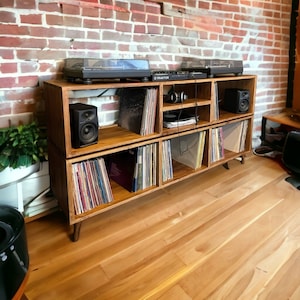 May include: A wooden record player stand with four shelves. The top shelf has a record player on it. The other shelves are filled with records. There are two speakers on the stand.