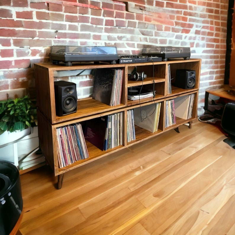 May include: A wooden record player stand with four shelves. The top shelf has a record player on it. The other shelves are filled with records. There are two speakers on the stand.
