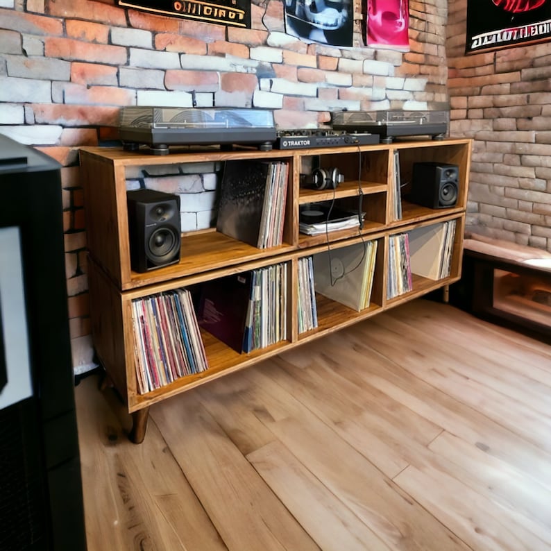 May include: A wooden record player stand with multiple shelves, filled with vinyl records. The stand has a dark brown finish and is made of solid wood. The stand is sitting on a light wood floor.