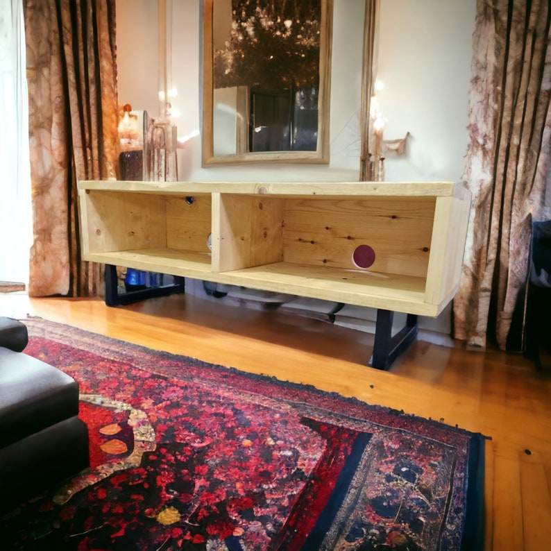 May include: A light wood entertainment center with three shelves and black metal legs. The unit is sitting on a red and black patterned rug.
