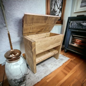 Könnte beinhalten: Eine Holzaufbewahrungsbank mit einem Klappdeckel und einem Regal. Die Bank ist aus Naturholz mit rustikalem Finish.
