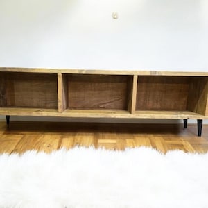 May include: A rustic wooden shelf unit with three open compartments. The shelf has a natural wood finish and black metal legs.