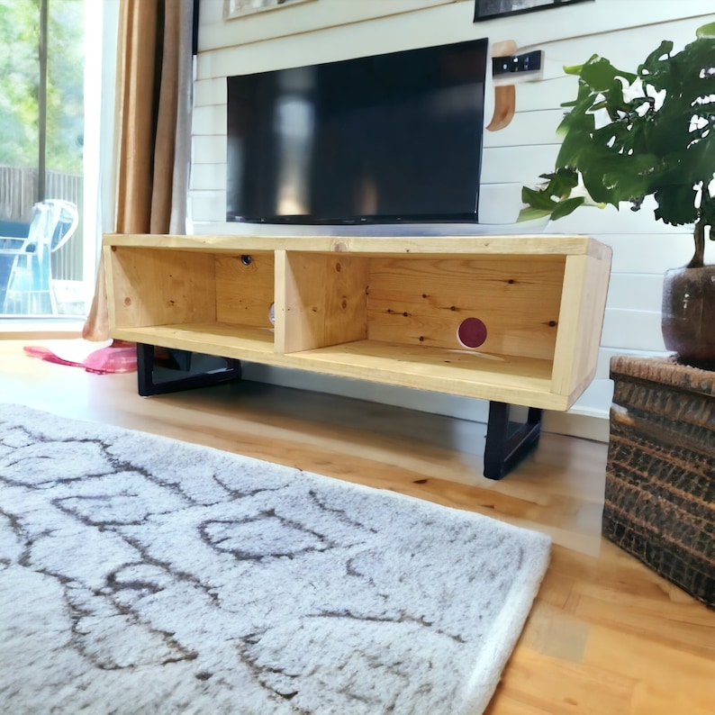 May include: A wooden TV stand with two shelves and black metal legs. The stand is made of natural wood with a light brown finish. The stand is sitting on a light brown wood floor.