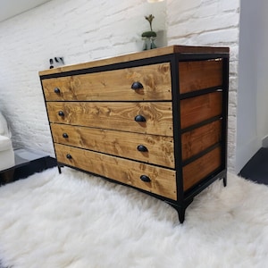 May include: A four-drawer dresser with a black metal frame and wooden drawers. The dresser has a rustic, industrial style and is sitting on a white fluffy rug.