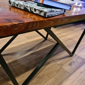 Puede incluir: Una mesa de centro de madera con un acabado marrón oscuro brillante y patas de metal negro. La mesa tiene un diseño único en forma de X para las patas.