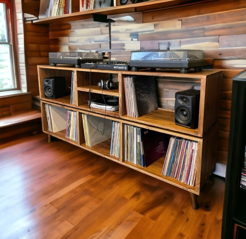 May include: A wooden record player stand with multiple shelves, featuring a turntable and speakers. The stand is made of light brown wood and has a rustic look. The shelves are filled with vinyl records.