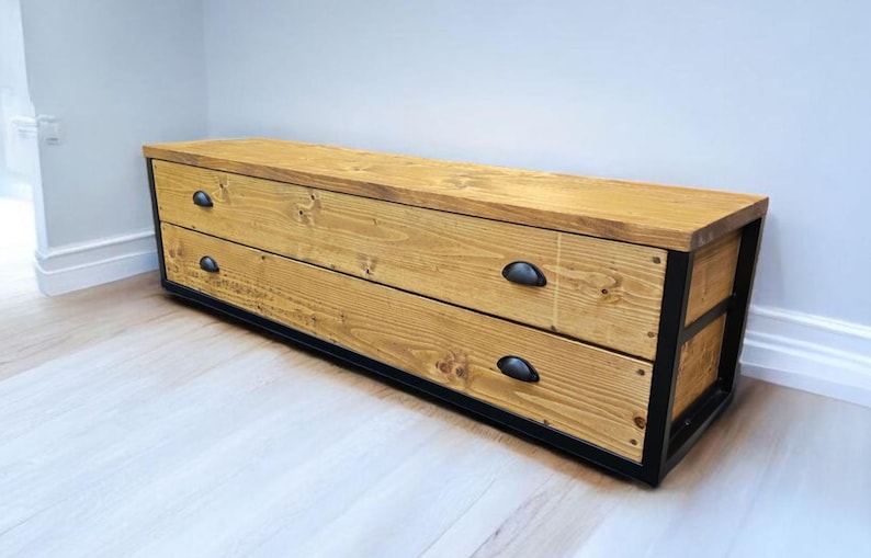 May include: A long wooden chest with two drawers and black metal accents. The chest has a natural wood finish and black metal drawer pulls.