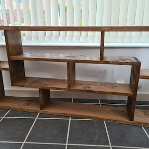 May include: A rustic wooden shelf unit with a unique asymmetrical design. The shelf has multiple compartments of varying sizes, perfect for displaying books, plants, or decorative items.