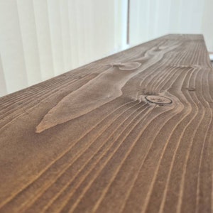 May include: Close-up of a dark brown wooden plank with a natural wood grain pattern and a knot in the center.