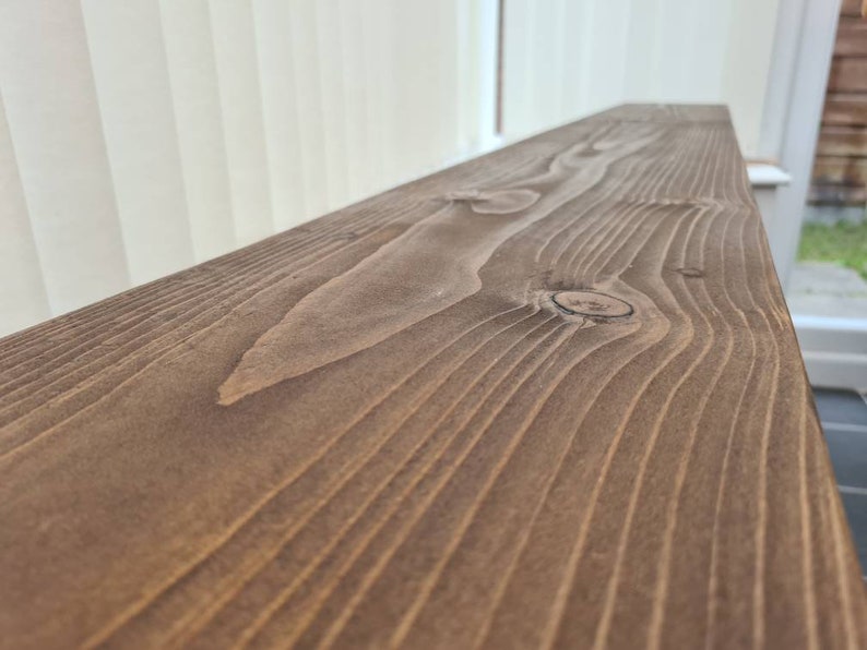 May include: Close-up of a dark brown wooden plank with a natural wood grain pattern and a knot in the center.