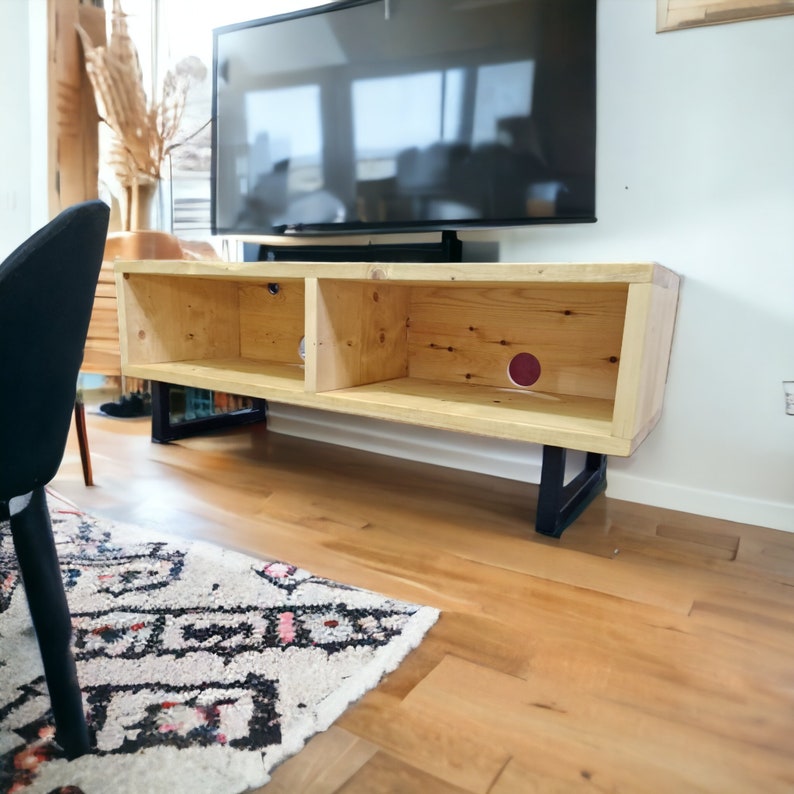 May include: A wooden TV stand with two shelves and black metal legs. The stand is made of natural wood with a light brown finish. The stand is sitting on a hardwood floor.