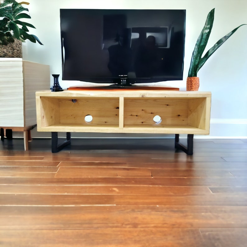 May include: A light wood TV stand with two open shelves and black metal legs. The stand is holding a flat screen TV and a small decorative object.