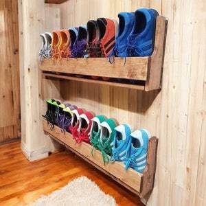 May include: A wooden shoe rack with two shelves mounted on a wall. The shelves are filled with a variety of colourful sneakers, including blue, green, red, orange, and purple.