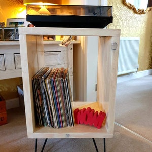 May include: A white wooden record player stand with hairpin legs. The stand has a shelf for records and a top shelf for a record player. The stand is decorated with a red "WOW!" sign.